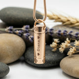 Rose gold Belle Fever Cylinder Cremation Necklace resting on stones — a beautifully handcrafted piece to cherish and remember loved ones forever