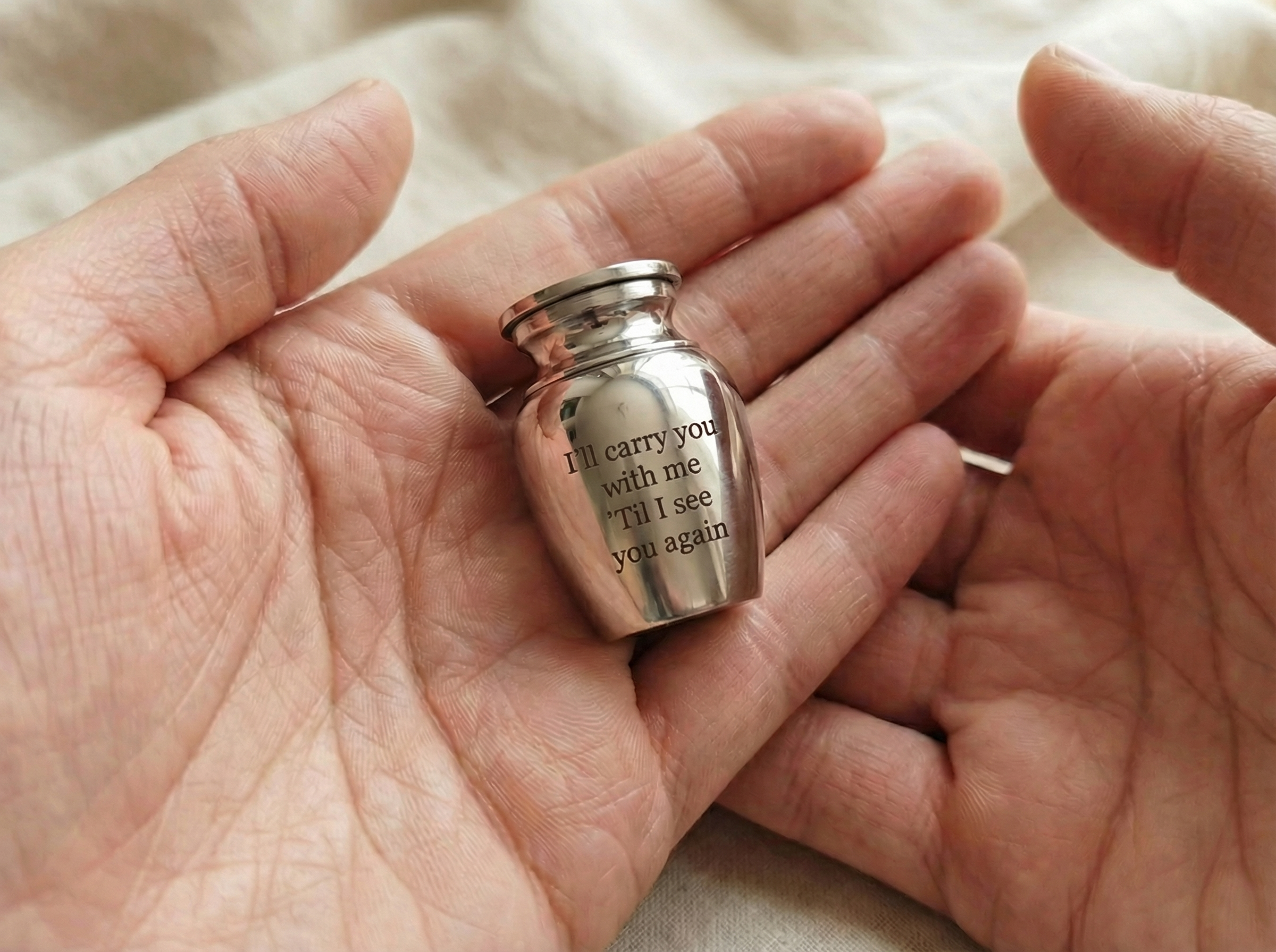 Small silver urn held in hands with engraved text