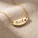 Gold Beck name necklace with engraved bar pendant and birthstone displayed on neutral fabric background