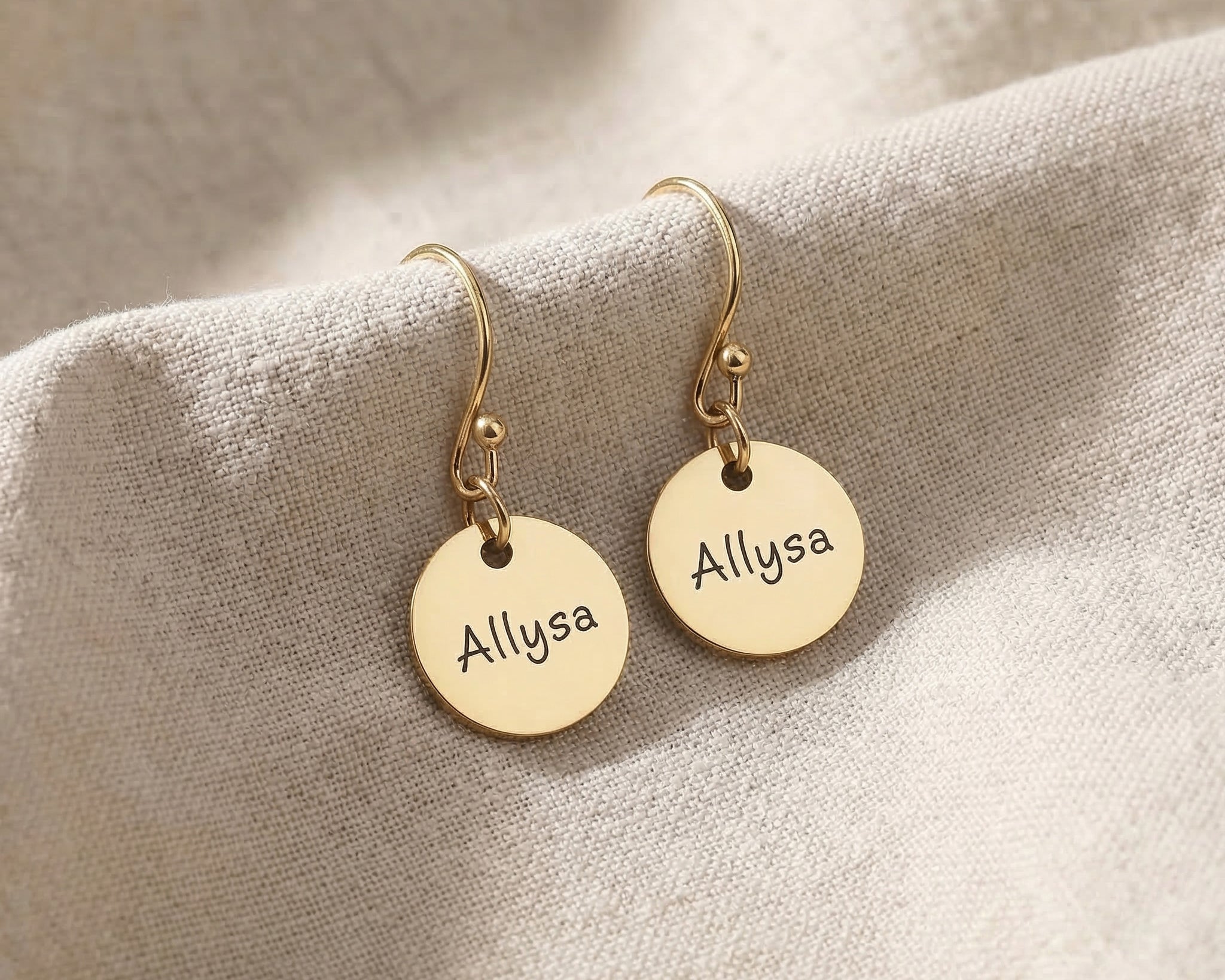 Gold personalised earrings with engraved name on disc design displayed on neutral background