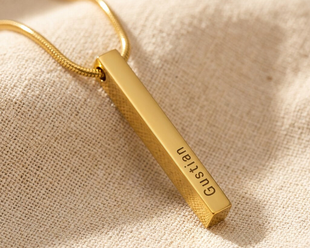 Gold vertical bar necklace with engraved bar pendant displayed on neutral background